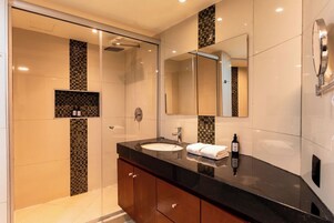 Un baño moderno con cabina de ducha de vidrio, un lavabo con encimera negra y un espejo sobre el lavabo.
