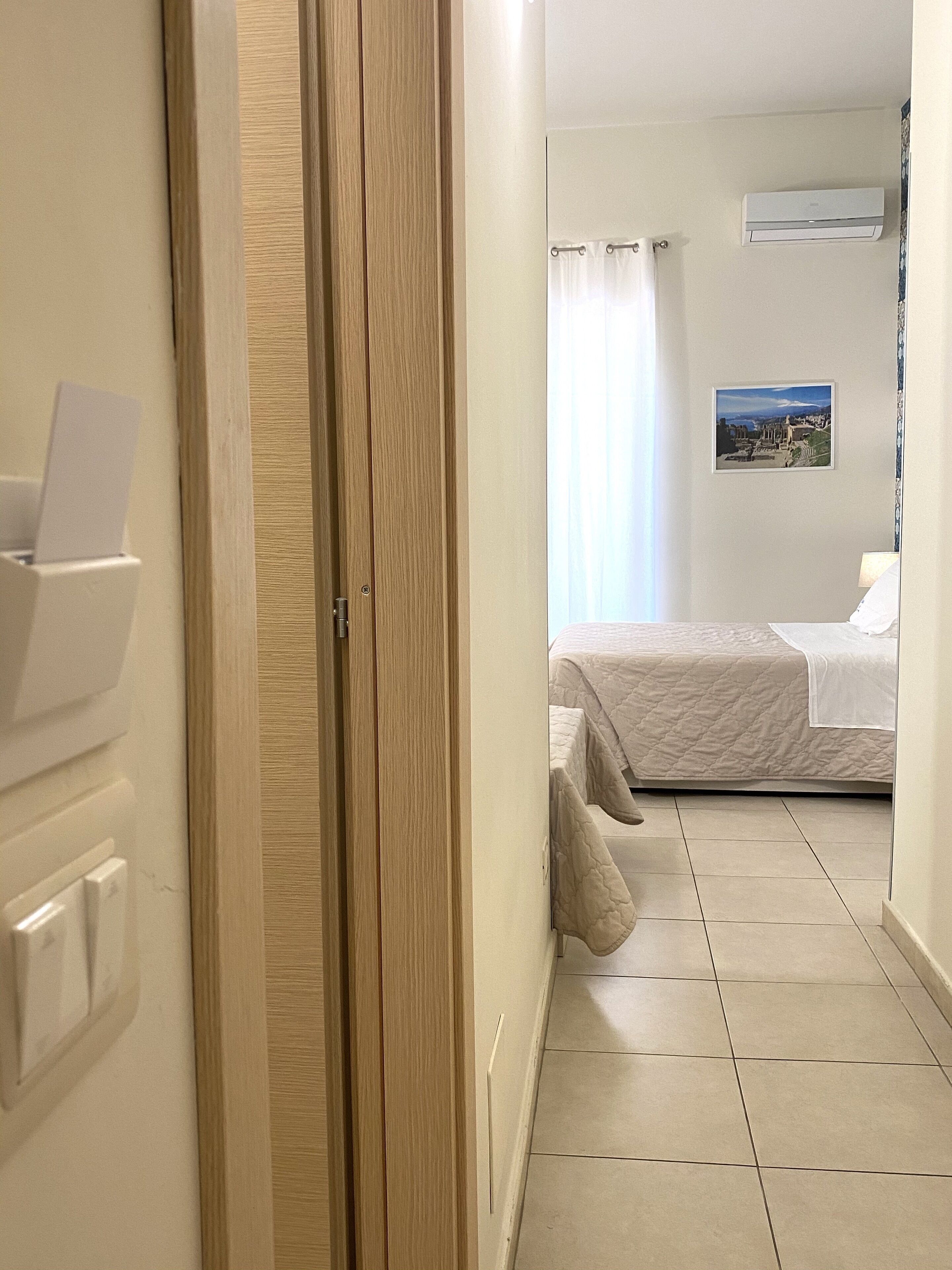 Une chambre d’hôtel comprenant un lit, une table de chevet, un climatiseur fixé au mur et une fenêtre avec des rideaux.