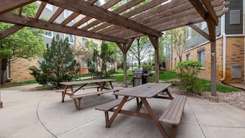 An outdoor patio area with wooden picnic tables and a grill.