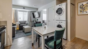 A compact living space with a dining area, a washing machine, and a TV mounted on the wall. - WaterWalk Extended Stay by Wyndham Wichita (Wichita)