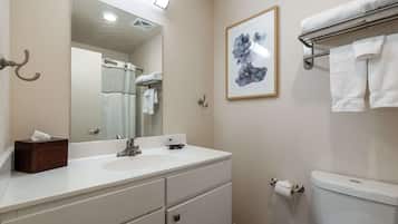 A bathroom with a white sink, mirror, and toilet. There is a towel rack with a towel on it, and a framed picture on the wall.