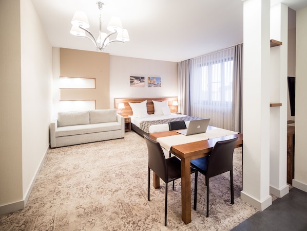 Quarto de hotel com uma cama, uma escrivaninha com um laptop, um sofá e um candelabro.