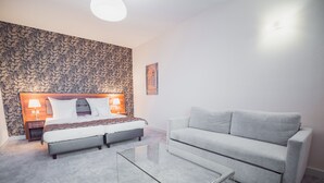 A modern bedroom with a bed, a sofa, a glass coffee table, and a patterned wallpaper. - Hotel Miodowa (Kraków)