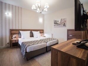 Quarto de hotel com cama de madeira, mesas de cabeceira, escrivaninha e televisão.