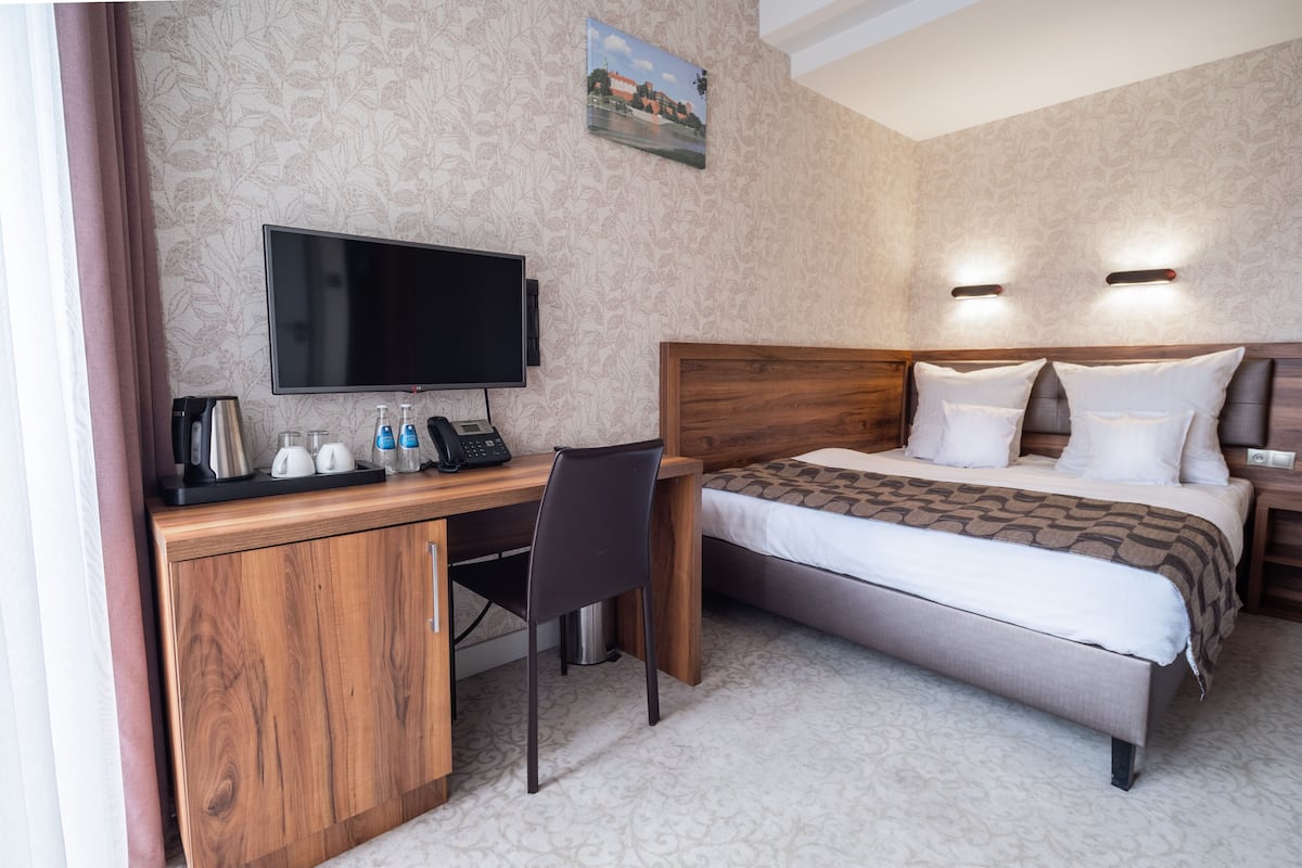 Quarto de hotel com escrivaninha de madeira, televisão de tela plana, cama com roupa de cama branca e carpete estampado.