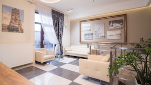 A hotel lobby with a checkered floor, two sofas, a glass table, a large framed picture of a cityscape, and a potted plant. - Hotel Miodowa (Kraków)