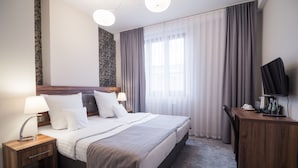 A hotel room with a large bed, bedside tables, a desk with a TV, and a window with curtains. - Hotel Miodowa (Kraków)