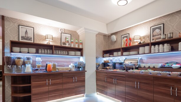 A well-lit breakfast bar with a variety of food and drink options, including cereals, fruits, and beverages. - Hotel Miodowa (Kraków)