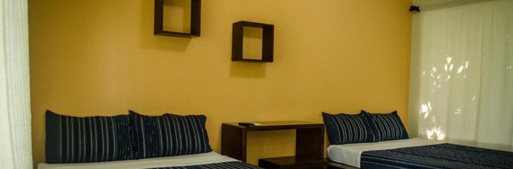 A hotel room with two beds, a small table, and a mirror on the wall.