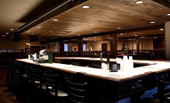 A bar area with a long counter, multiple stools, and a wooden ceiling. - Lake Harmony Inn (Lake Harmony)