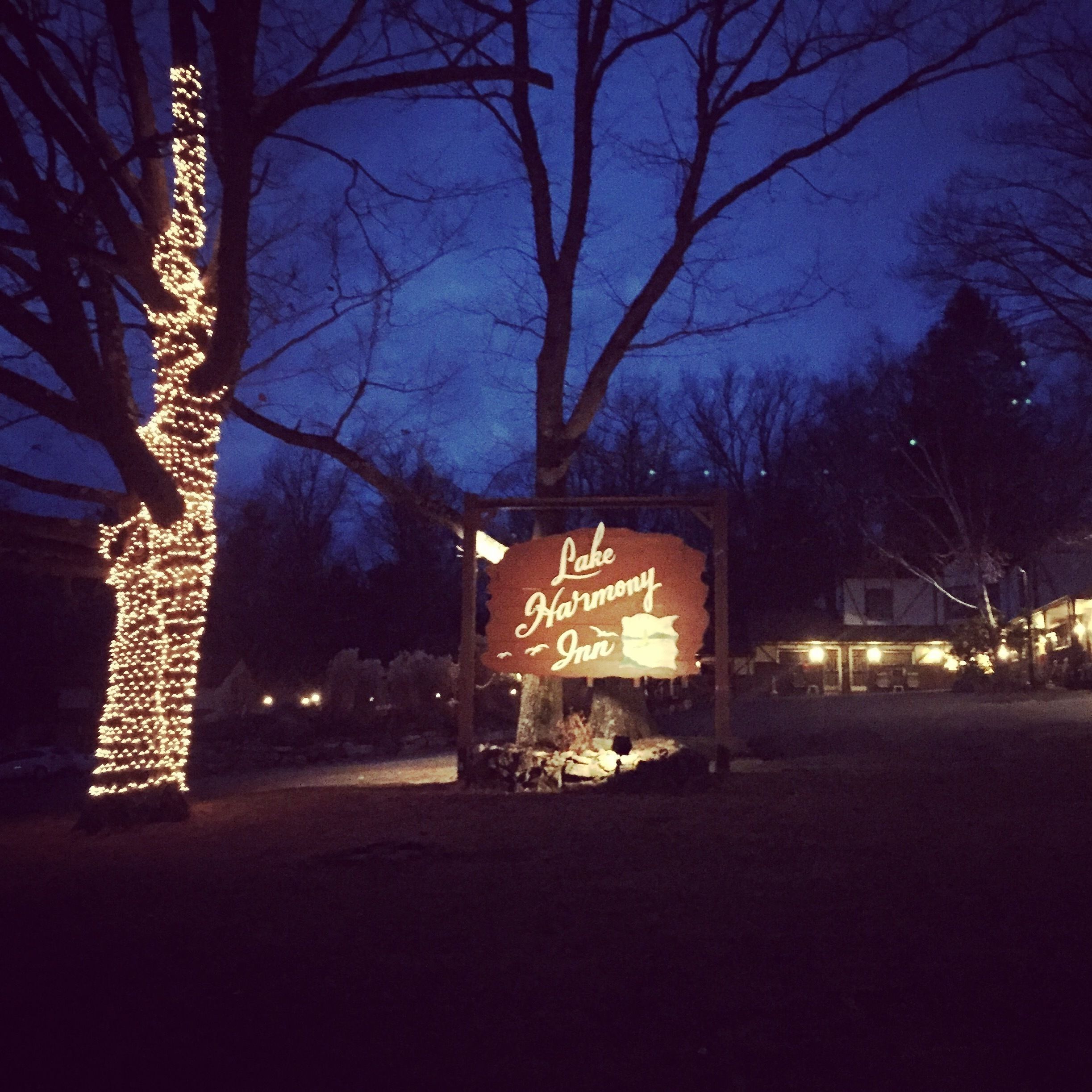 A sign for 'Lake Harmony Inn' with a rustic wooden structure and a tree decorated with lights.