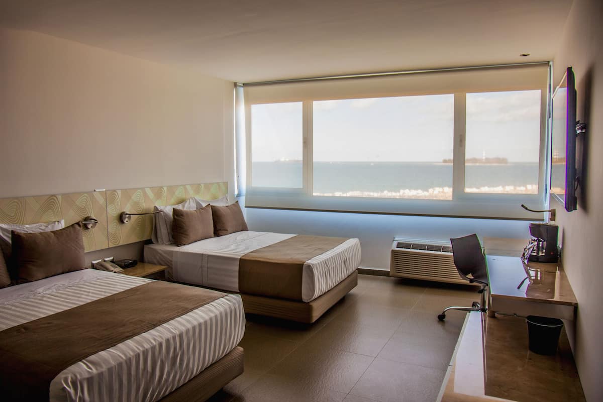 Une chambre d’hôtel avec deux lits, un bureau et une grande fenêtre donnant sur la mer.