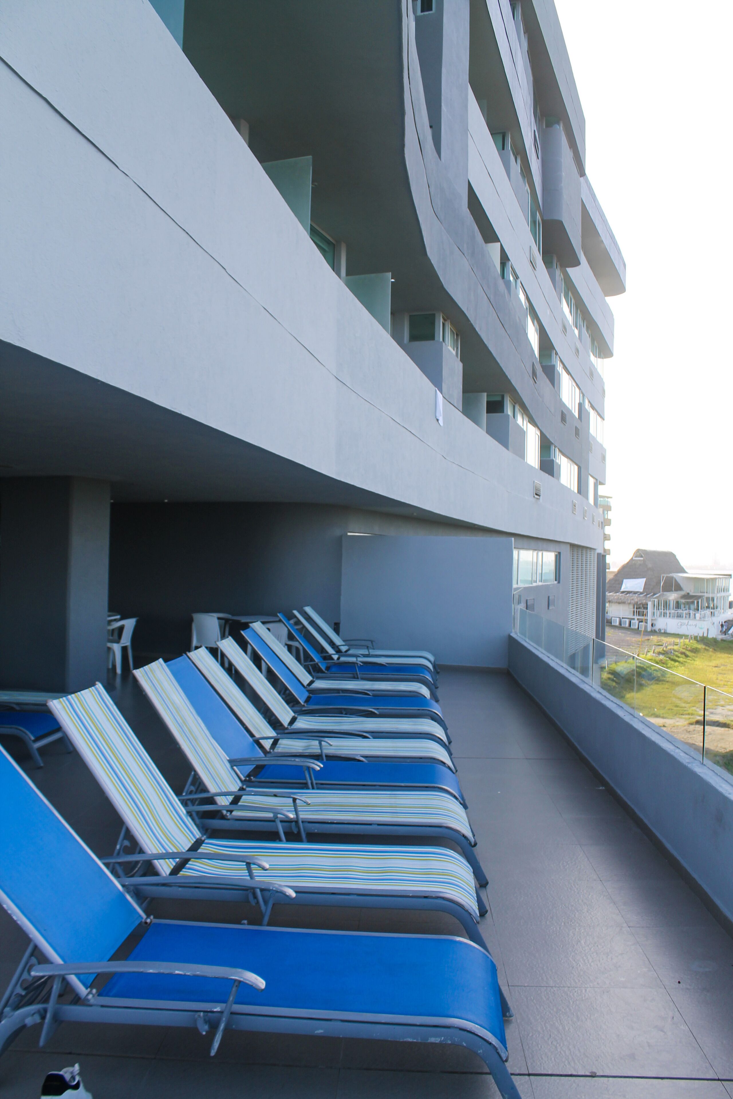 Un balcon avec plusieurs rangées de chaises longues bleues et, en arrière-plan, un bâtiment moderne.
