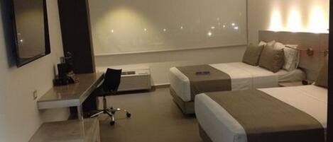 A hotel room with a desk, two beds, a chair, and a large window.