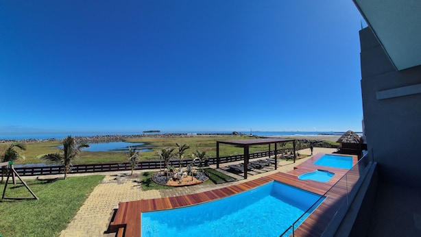 A pool area with two swimming pools, a wooden deck, and a view of the beach and ocean.