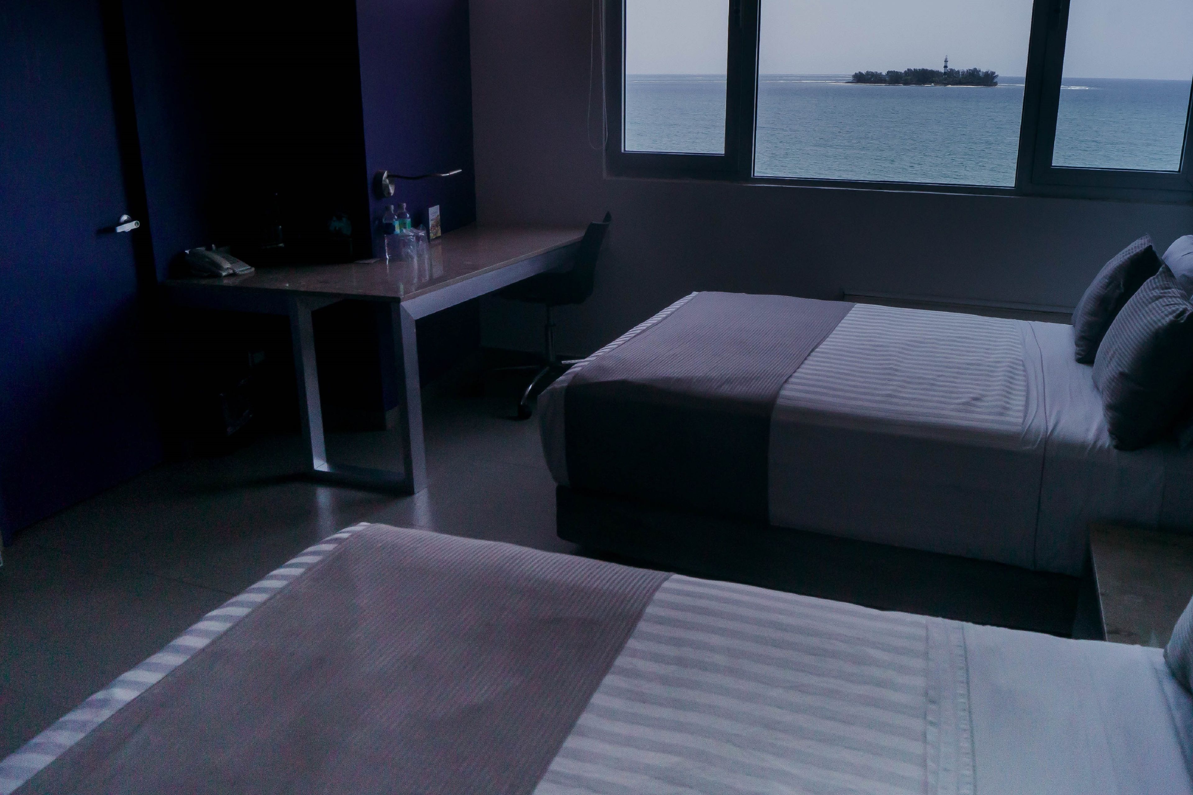 A hotel room with two beds, a desk, and a view of the sea.