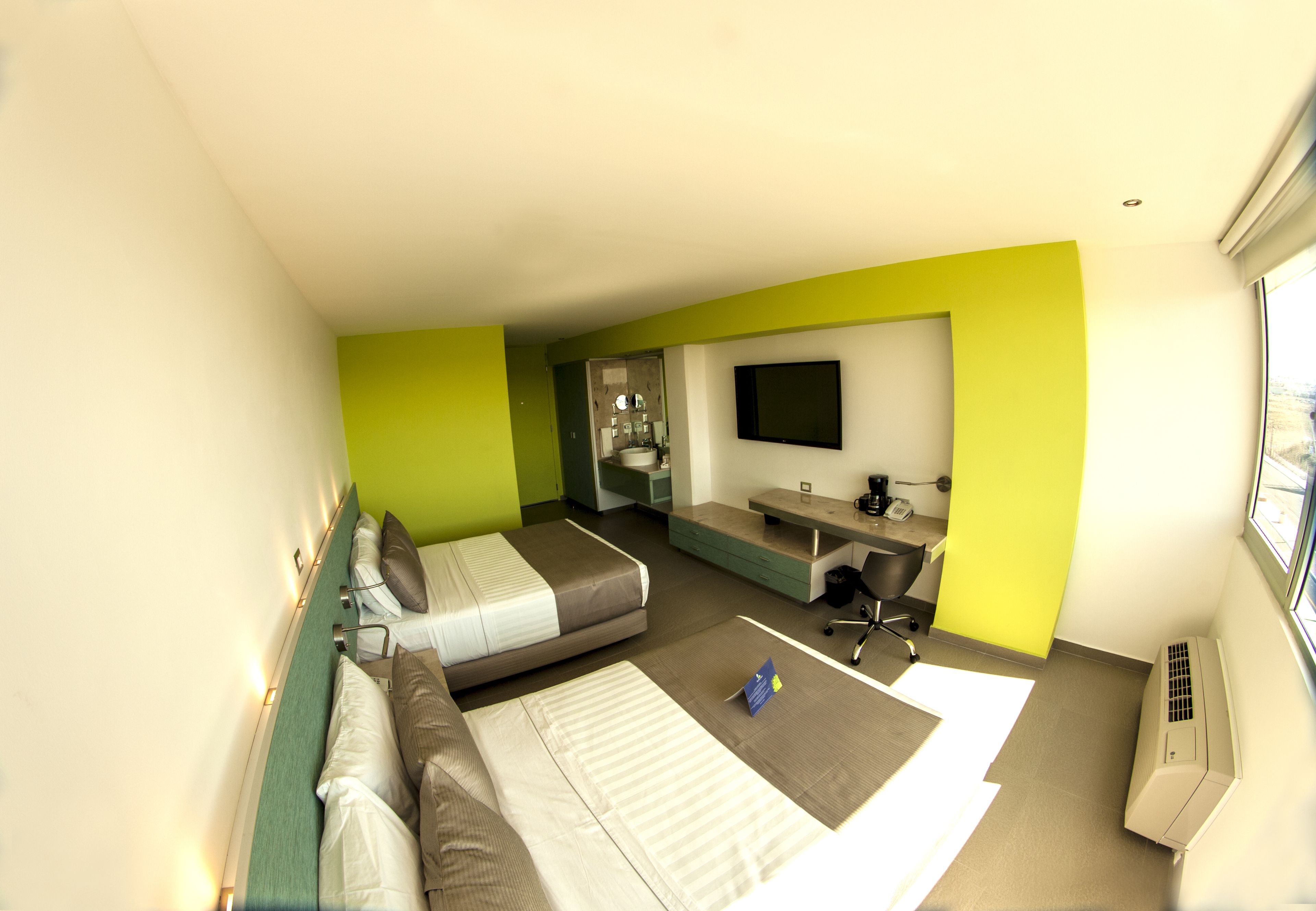 Una habitación de hotel con dos camas, un escritorio, una silla, un televisor y aire acondicionado.