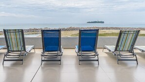A terrace with four lounge chairs facing a beach and ocean view.