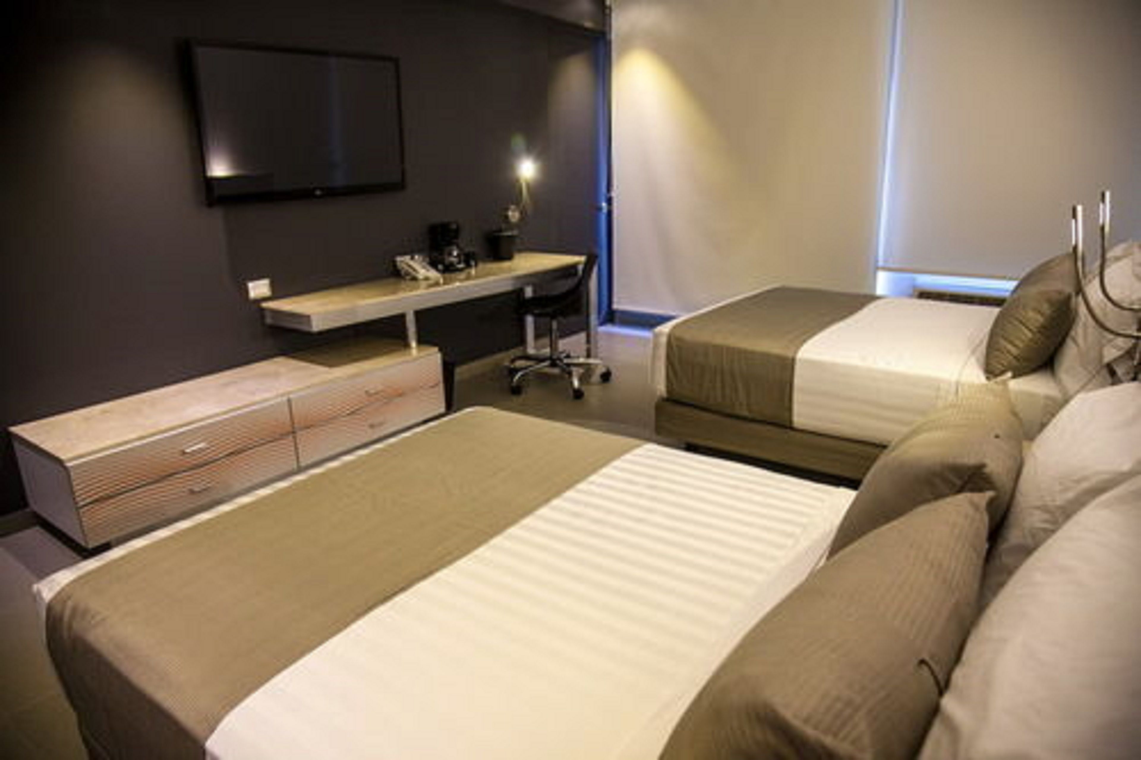 A hotel room with two beds, a desk, a chair, and a TV on the wall.