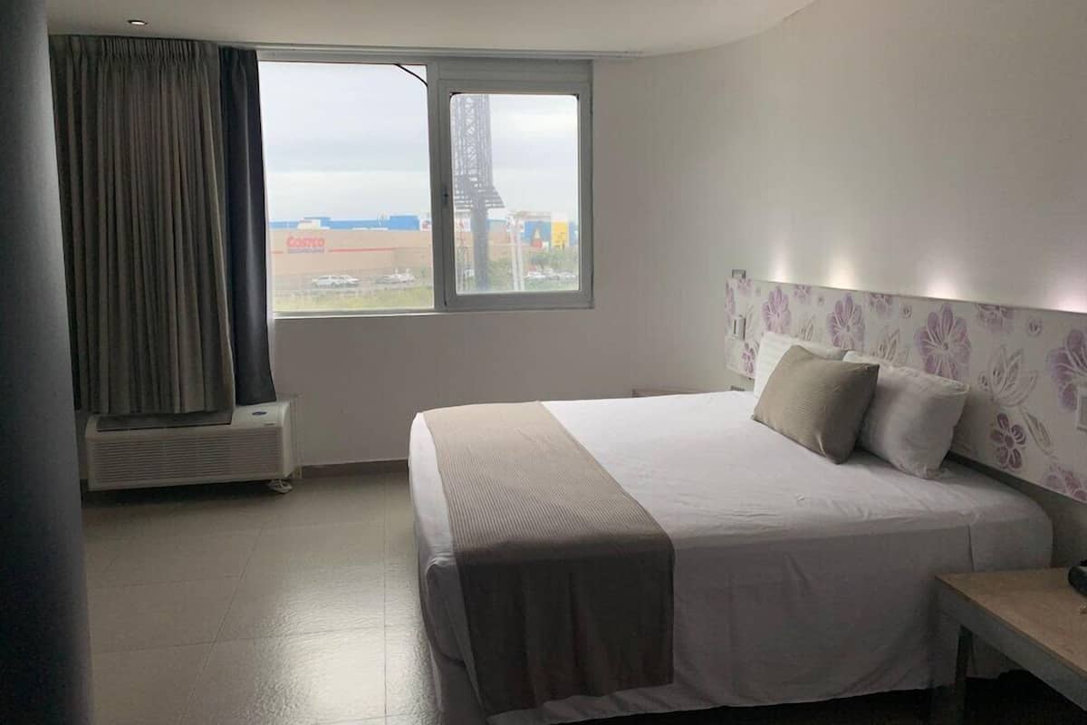 Une chambre d’hôtel avec un lit, une table de chevet, une fenêtre avec des rideaux et une vue sur un bâtiment à l’extérieur.