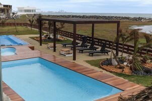 Una piscina con muelle de madera, sillas de descanso y vista a la playa.
