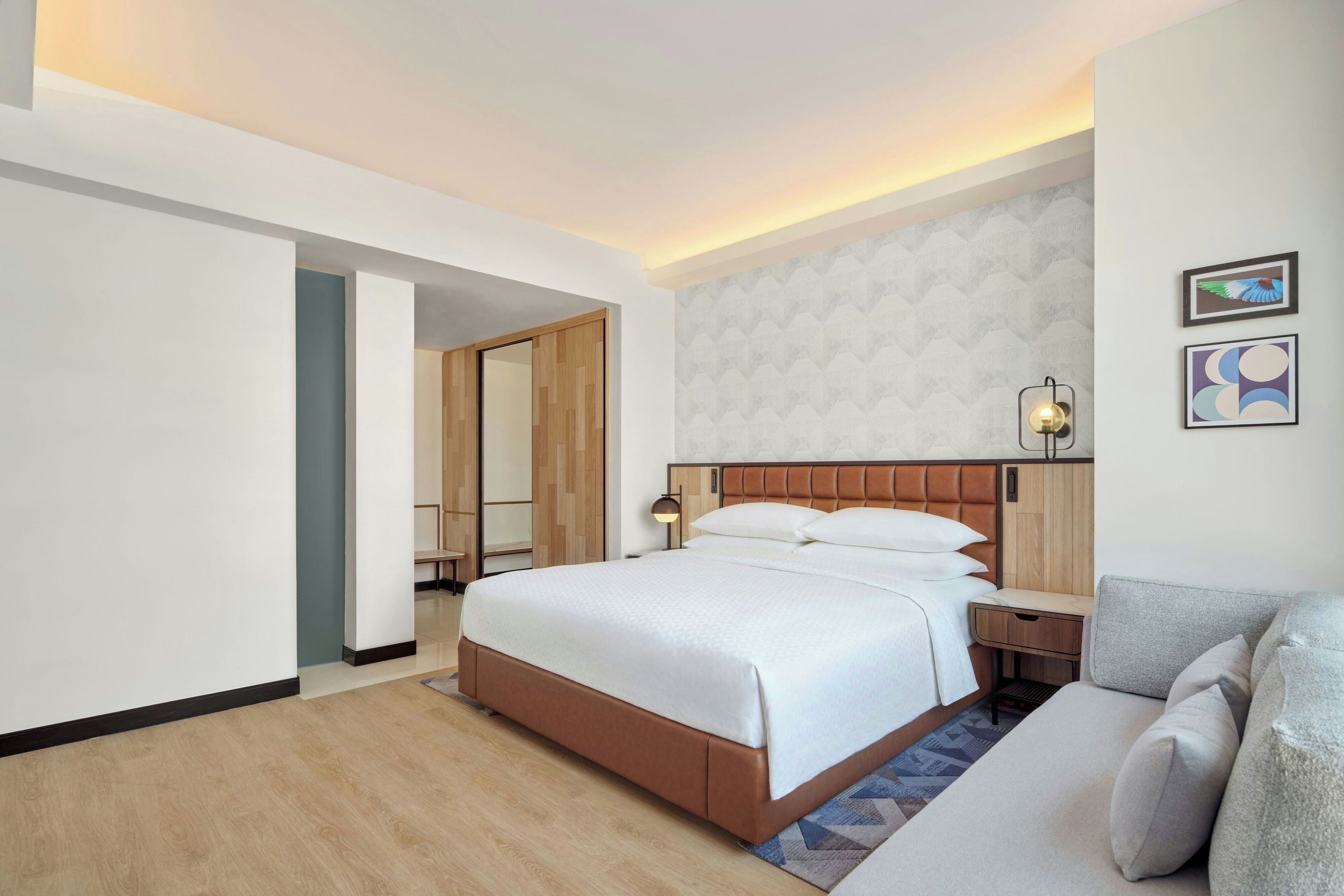 Una camera d'albergo con un letto, un comodino, una lampada, un divano e una parete decorata con due quadri.