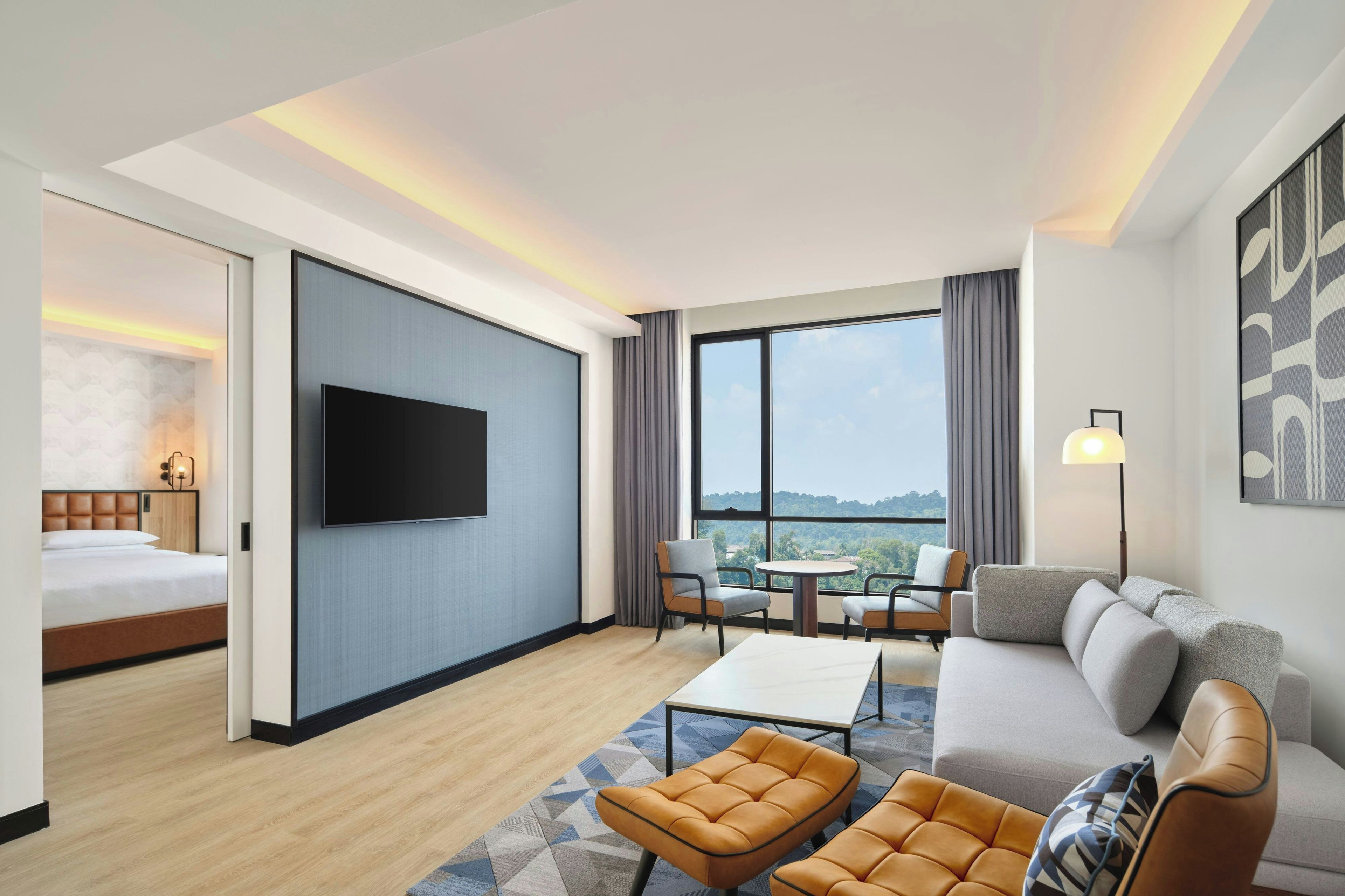 Habitación de hotel con cama, televisor, sofá, mesa de centro y vistas al exterior.