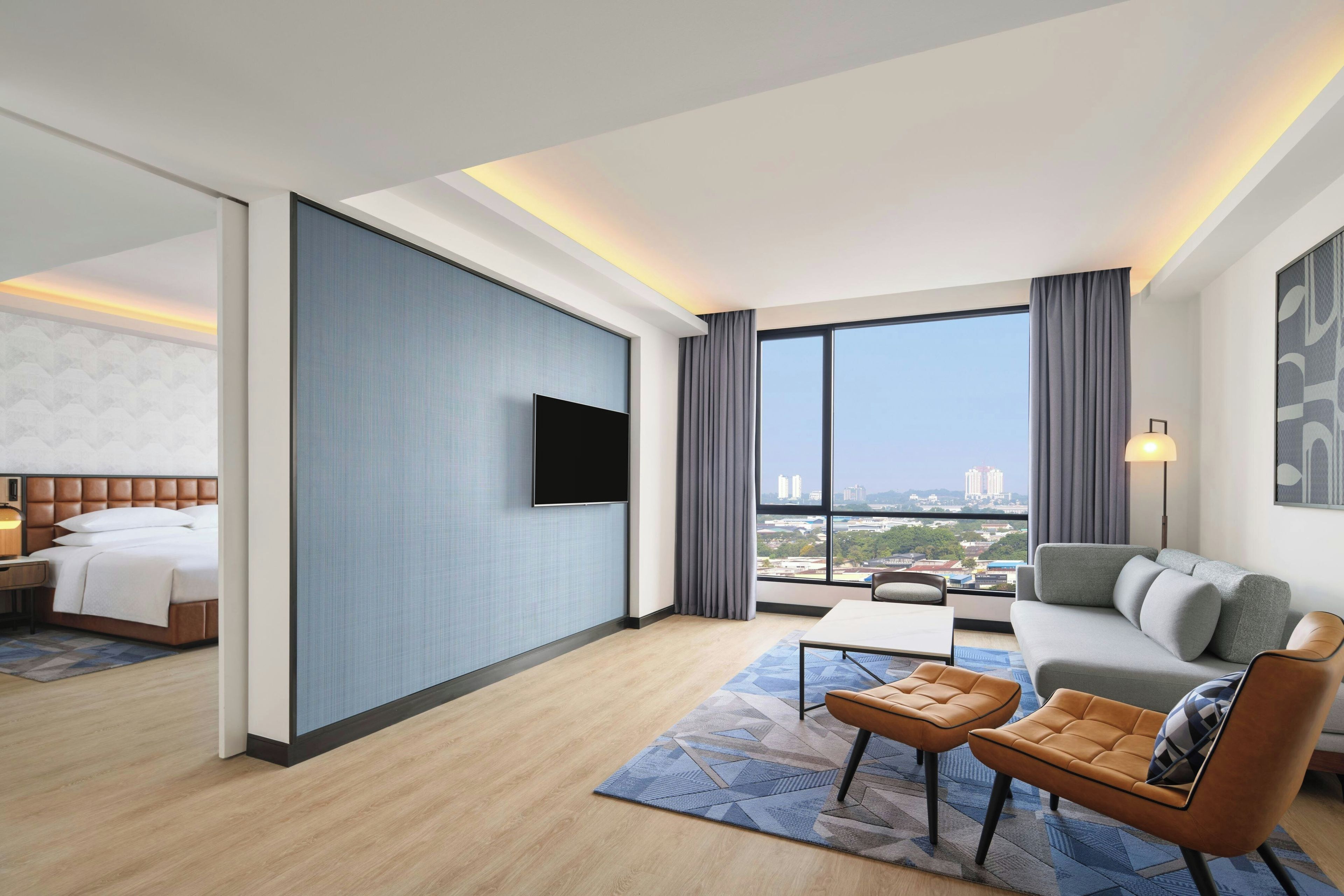 A hotel room with a bed, a TV, a sofa, a coffee table, and a view of the city.