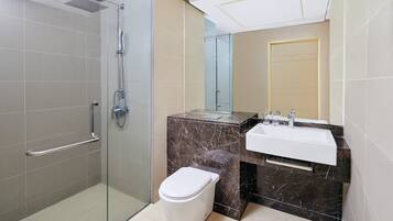 Un baño moderno con cabina de ducha de vidrio, inodoro blanco, lavamanos de mármol y espejo.