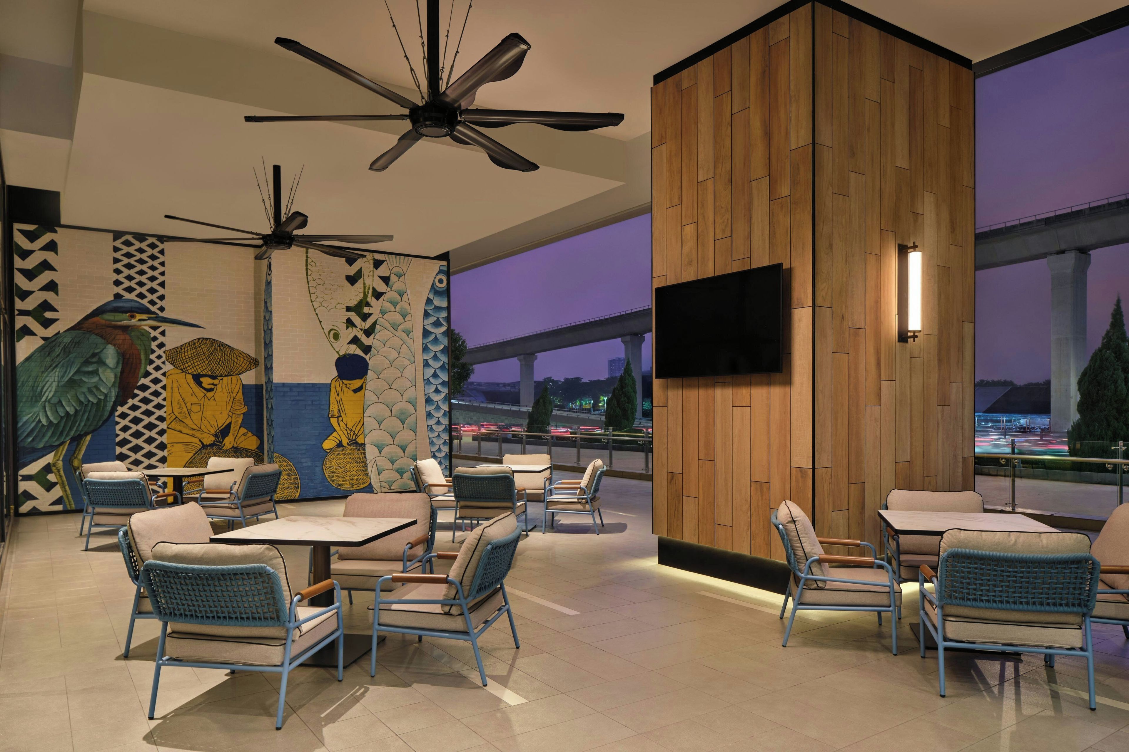 A modern restaurant interior with high ceilings, ceiling fans, and a large mural on the wall.