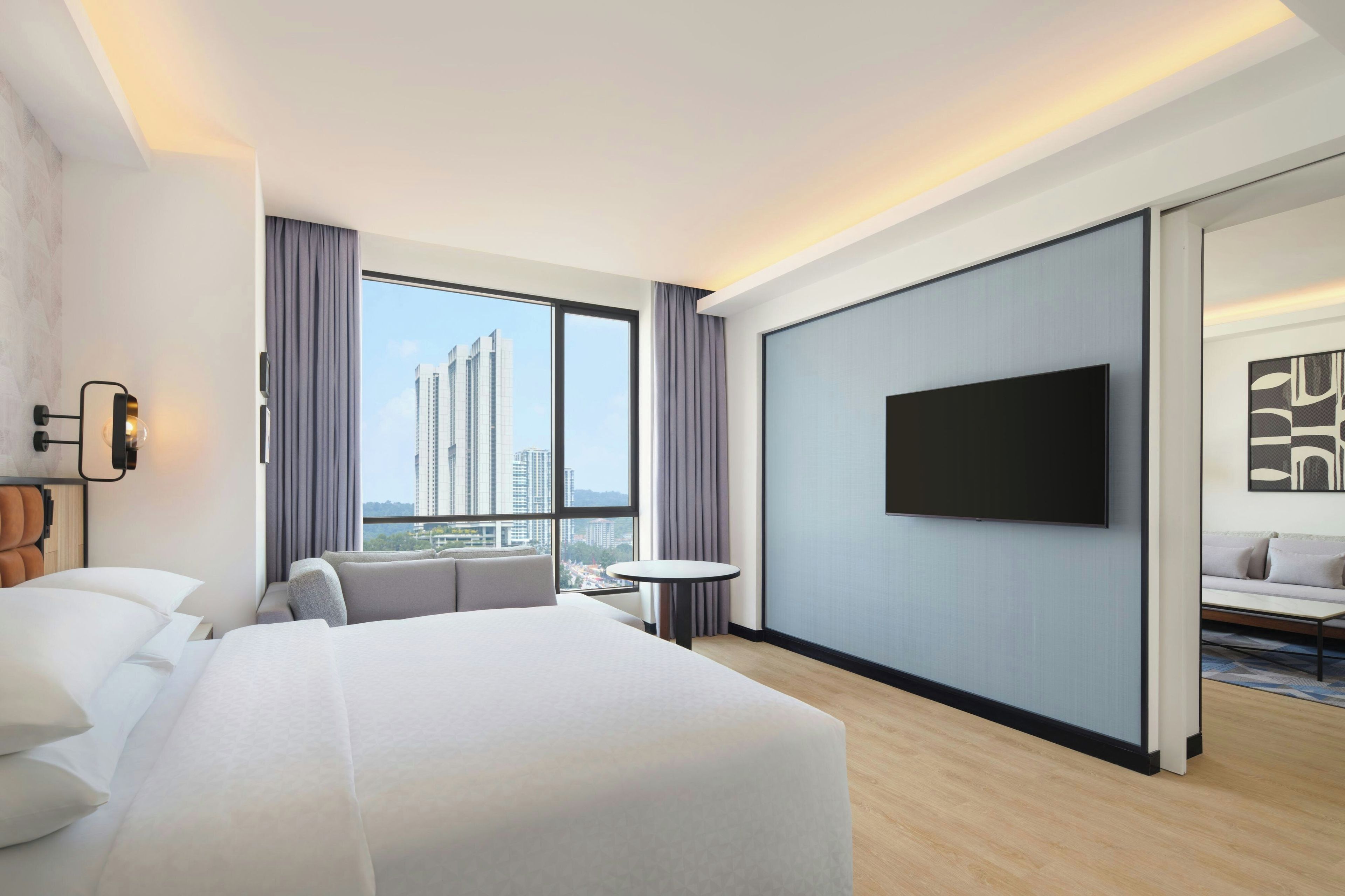 Habitación de hotel con cama, televisor, una mesita y vistas a edificios altos.