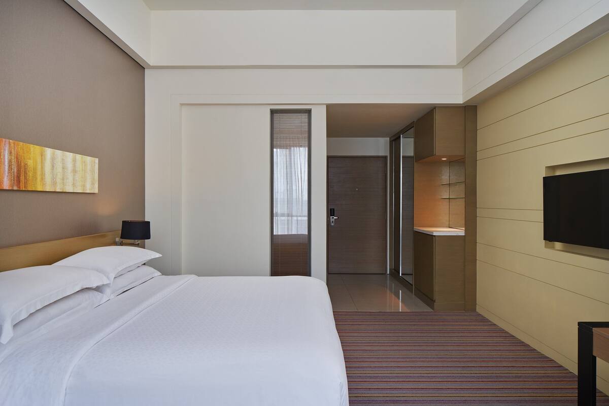 Ein Hotelzimmer mit einem großen Bett, einem Fernseher und einem durch eine offene Tür einsehbarer Badezimmer.