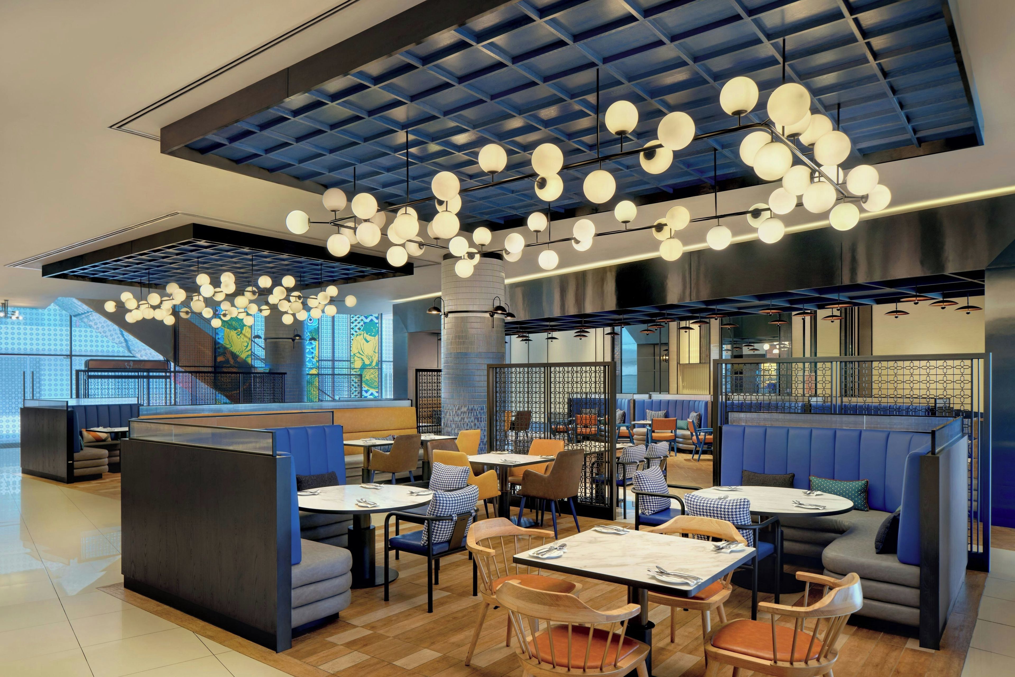 Un interior de restaurante moderno con techos altos, lámparas esféricas colgantes y una variedad de opciones de asientos, incluyendo cabinas y mesas.