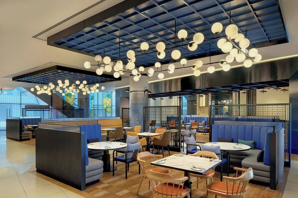 Un interior de restaurante moderno con techos altos, lámparas esféricas colgantes y una variedad de opciones de asientos, incluyendo cabinas y mesas.