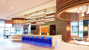Un área de bar moderna con techo alto, varios niveles y diversas opciones de asientos, como taburetes y sofás.