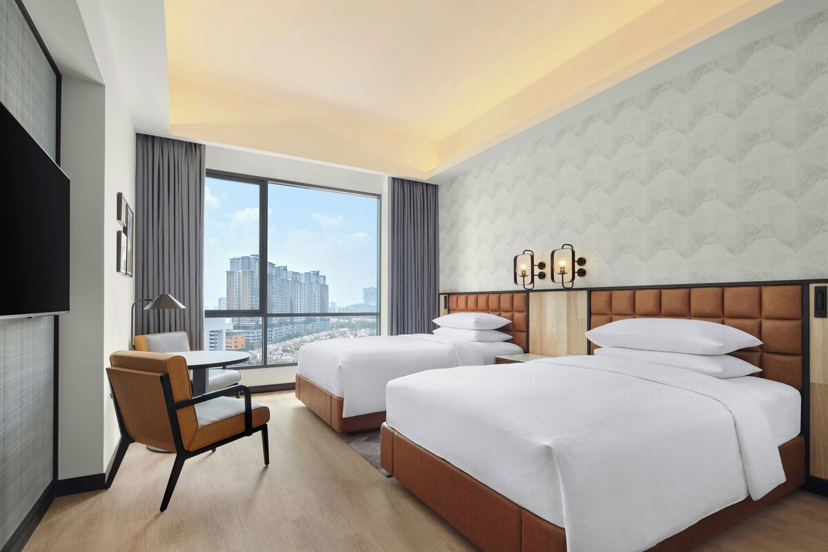 Habitación de hotel con dos camas, un escritorio, una silla, un ventanal grande con vista a la ciudad y un televisor de pantalla plana.