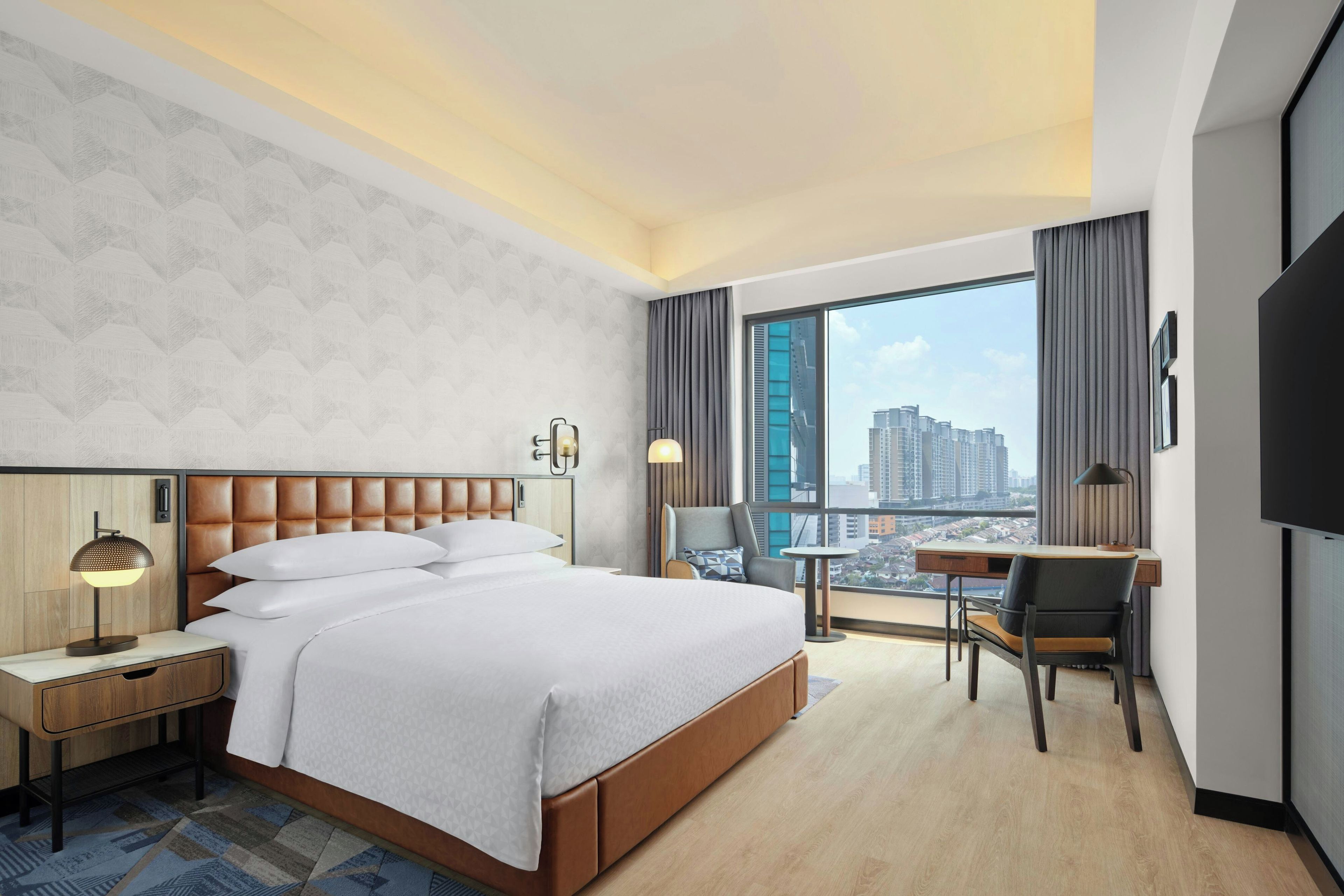 Moderni hotellihuone, jossa on suuri sänky, työpöytä ja näkymä kaupungin ylle.