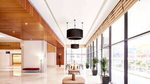 Un moderno vestíbulo de hotel con techo de madera, una recepción, área de descanso y amplios ventanales con vistas a la ciudad.