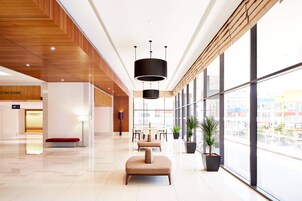 A modern hotel lobby with a wooden ceiling, a reception desk, seating area, and large windows offering a city view.