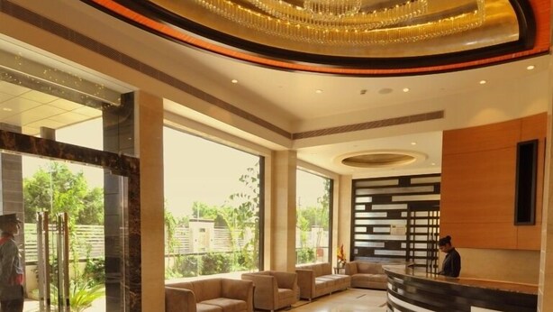 A modern lobby with a reception desk, comfortable seating, and large windows offering a view of greenery outside. - Hotel Marigold Jaipur (Jaipur)