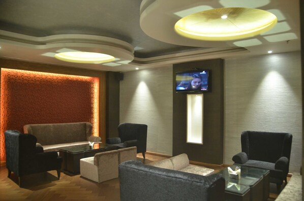 A modern lounge area with a sofa, armchairs, and a coffee table. A flat-screen TV is mounted on the wall.