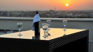 A table with four wine glasses and a bottle of wine, set against a sunset view. - Hotel Marigold Jaipur (Jaipur)