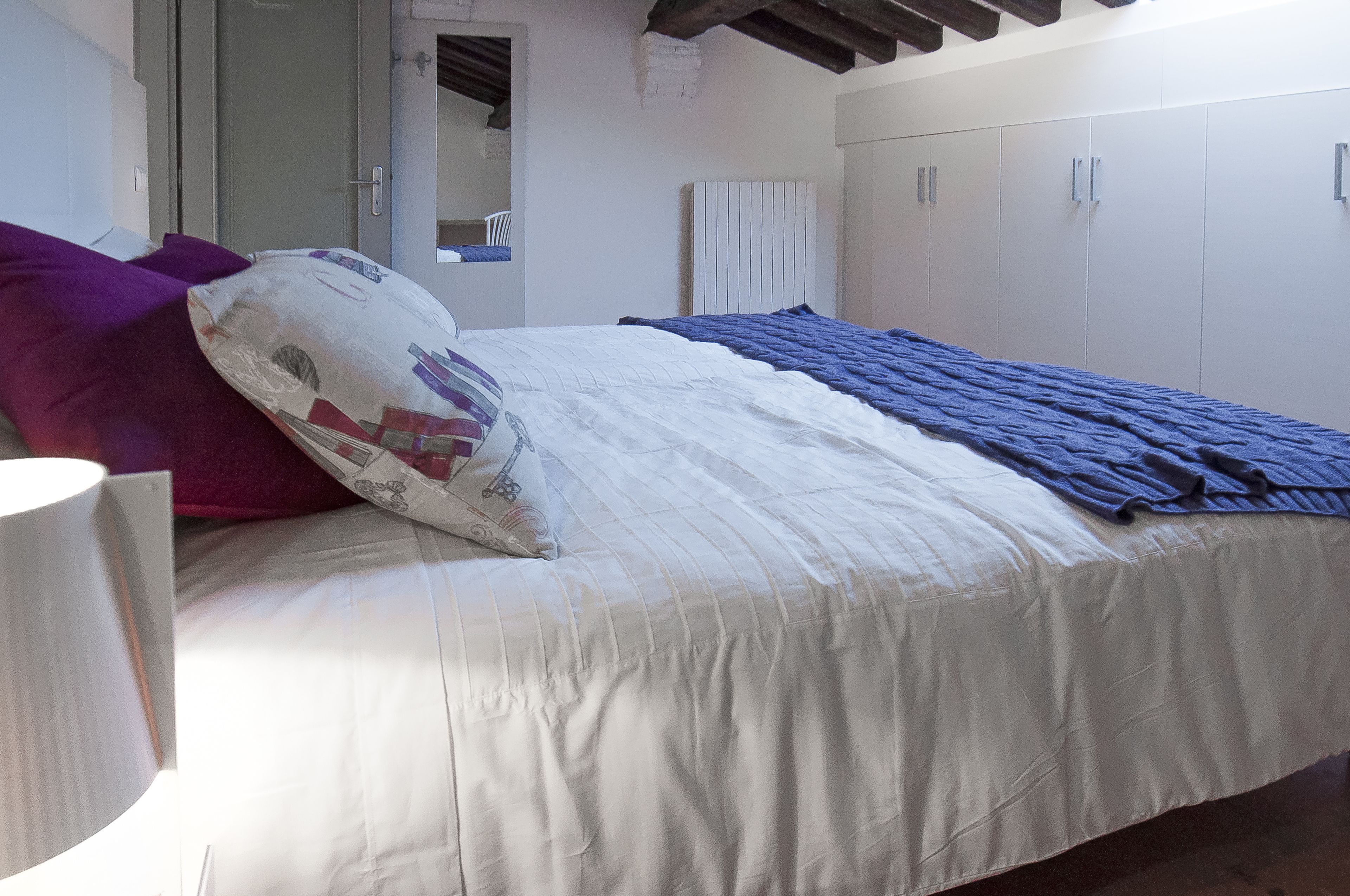 Quarto com cama, luminária de cabeceira, guarda-roupa e porta para outro cômodo.