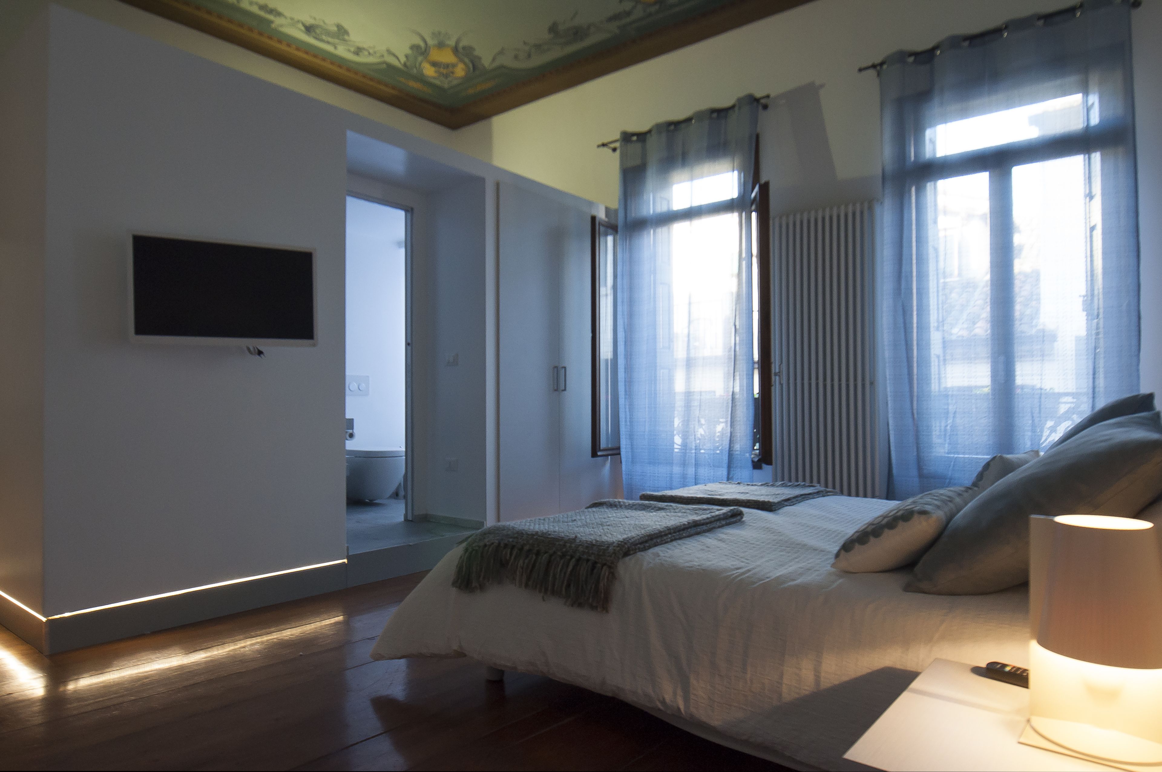 Une chambre à coucher avec un lit, un téléviseur fixé au mur et une fenêtre avec des rideaux.