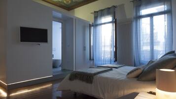 Une chambre à coucher avec un lit, un téléviseur fixé au mur et une fenêtre avec des rideaux.
