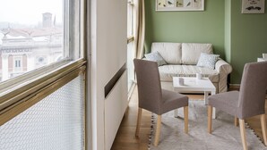 A room with a view of a building through a window, a sofa, two chairs, a small table, and a green wall with framed pictures. - B&B Scrovegni (Padova)