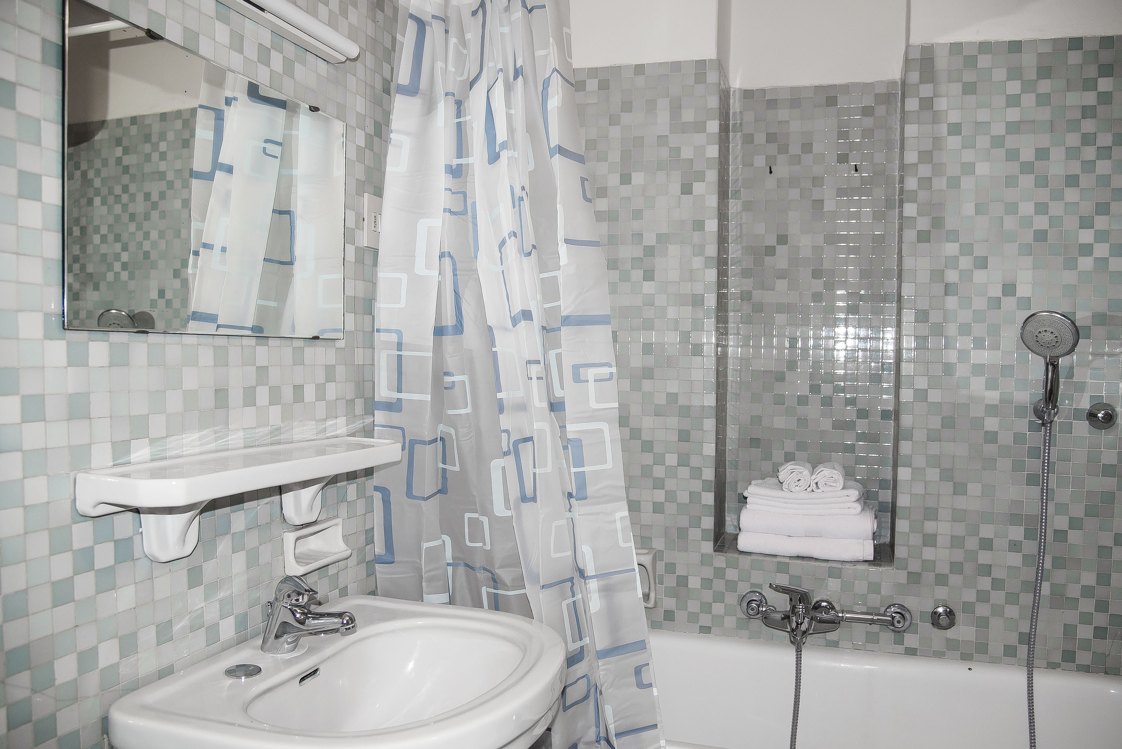 A bathroom with a sink, mirror, shower, and tiled walls.