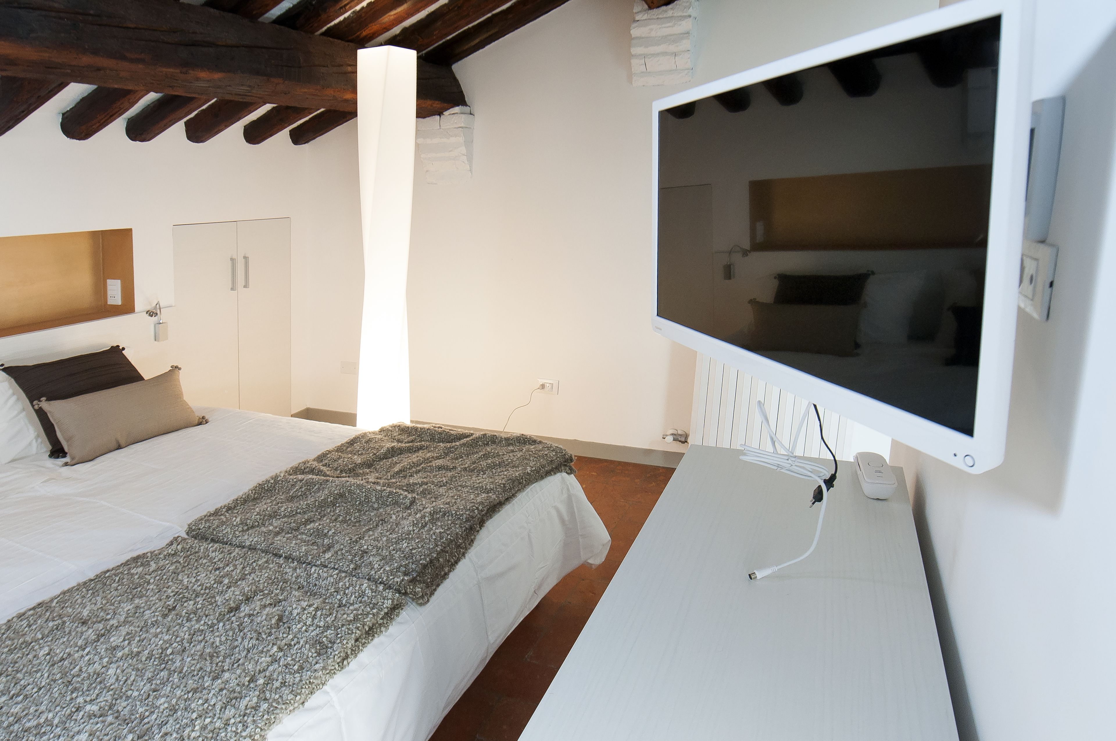 Quarto com cama, TV fixada na parede e teto de madeira.