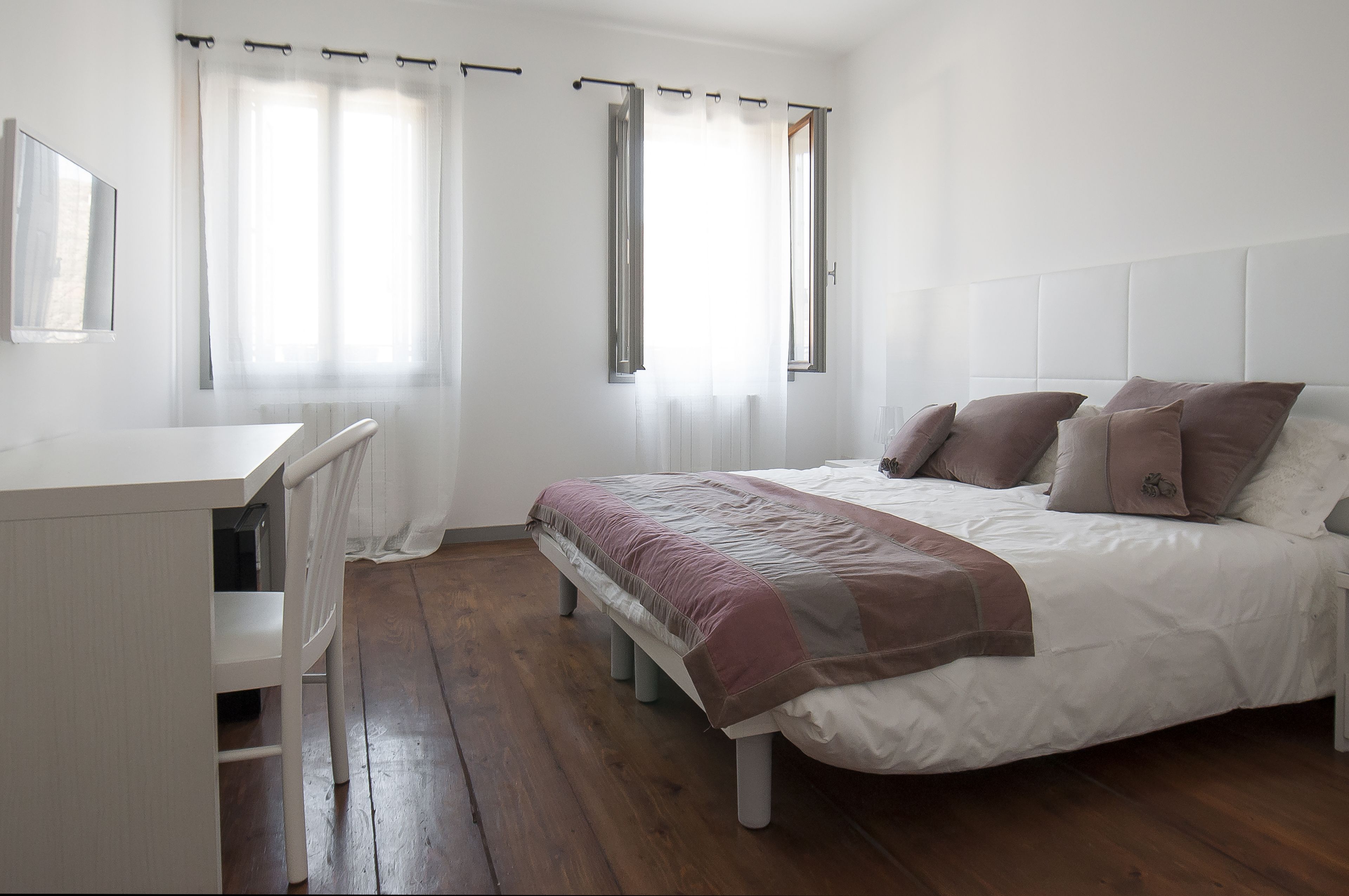Une chambre à coucher avec un lit, une table de chevet, une chaise et une fenêtre avec des rideaux.