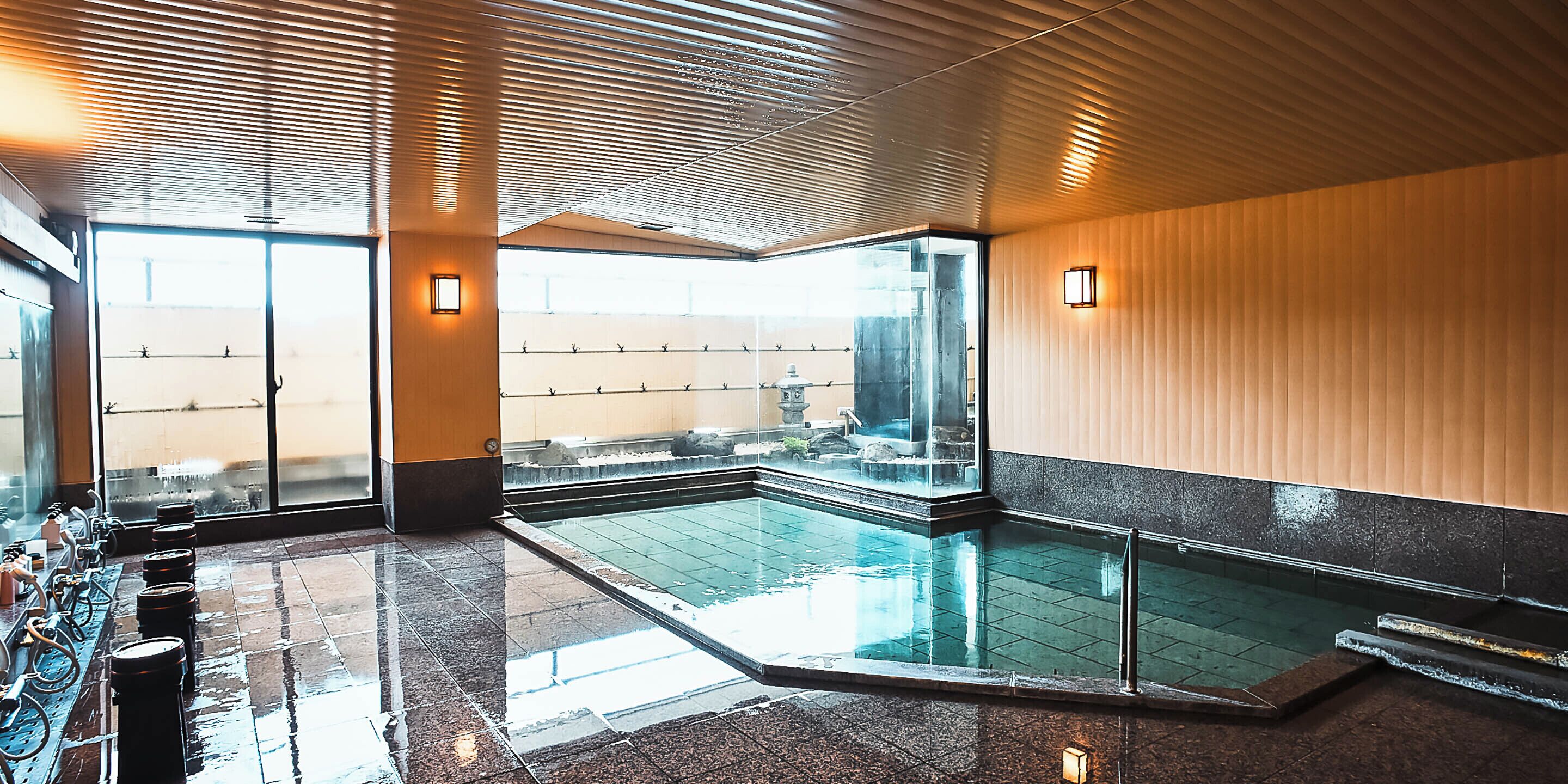 Un área de piscina interior moderna con paredes de vidrio transparente, suelo de baldosas y techo de madera.
